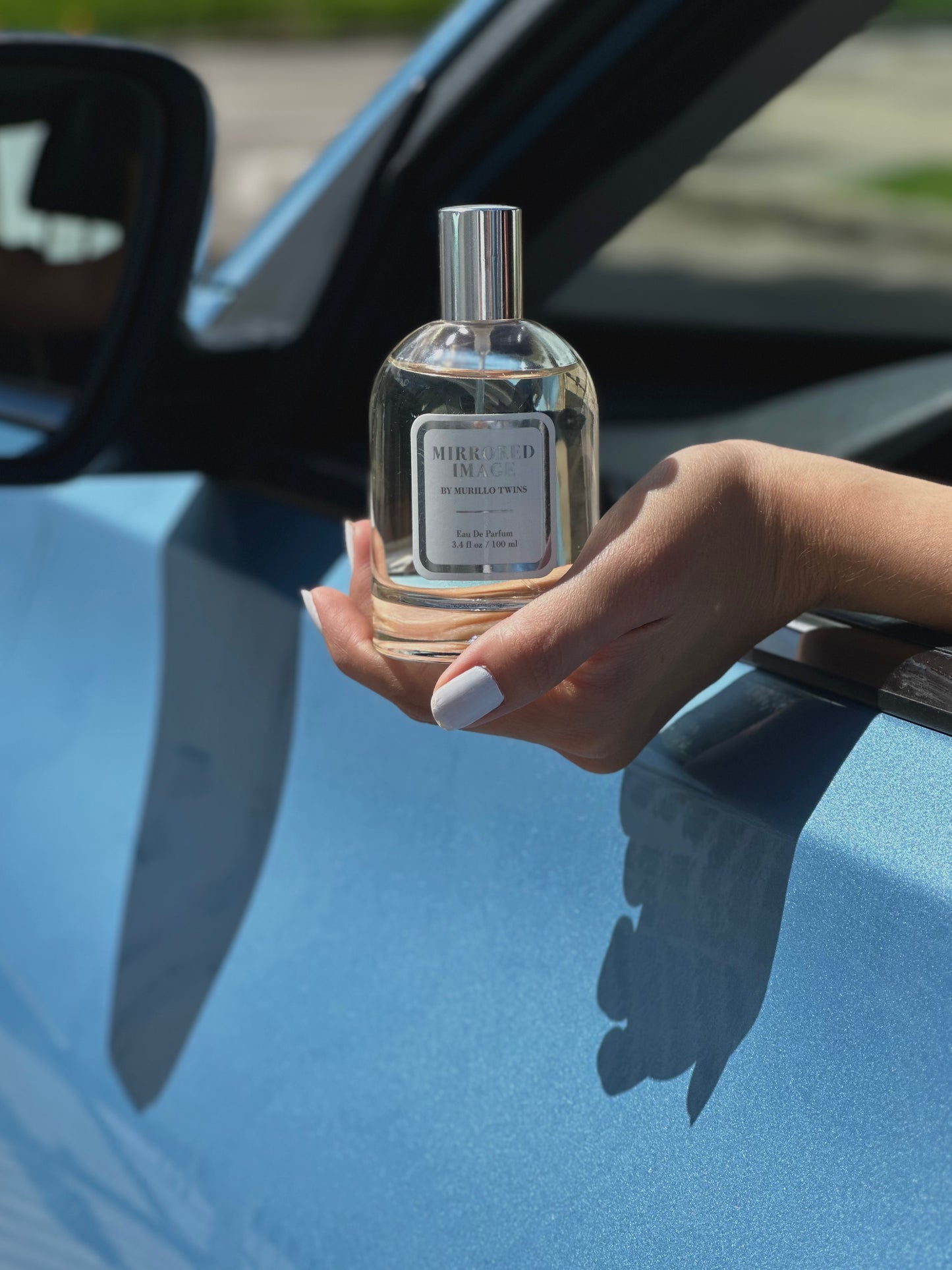 Someone holding the Mirrored Image Eau de Parfum just outside a car window.