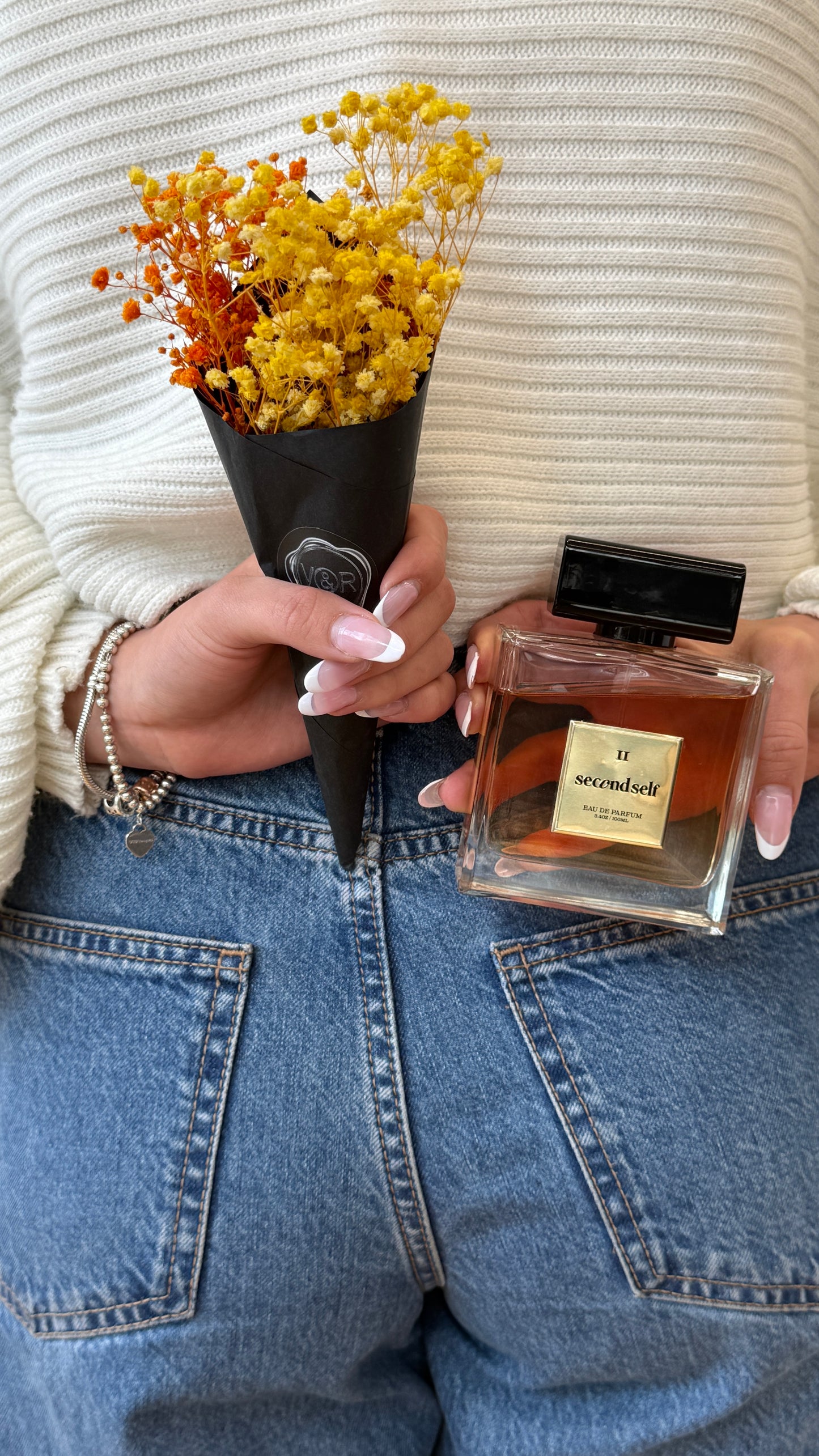 Someone holding the Second Self fragrance behind their back, hiding it alongside a bouquet of flowers.