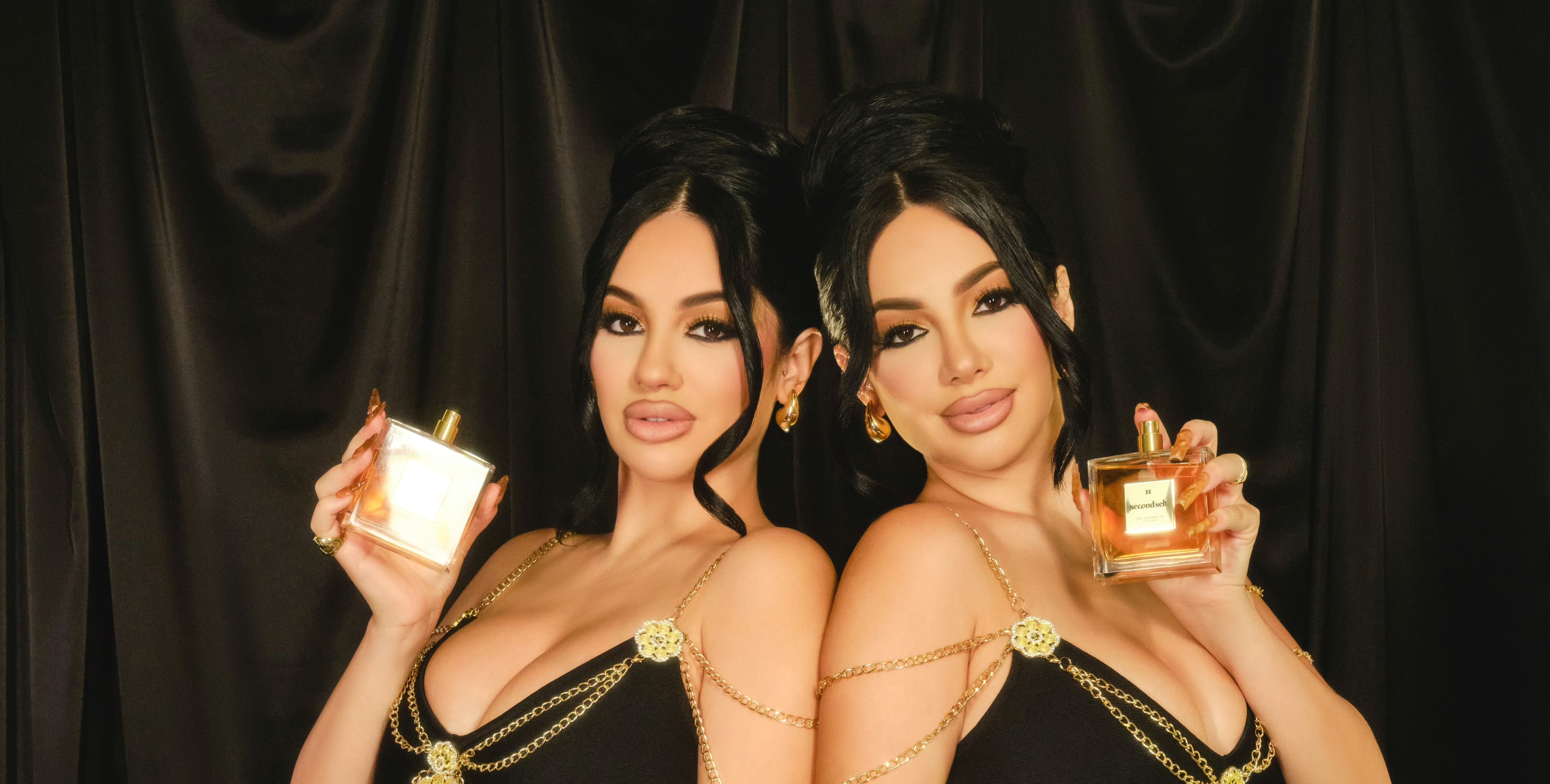 Brittany and Briana Murillo posing back to back, each holding a bottle of the Second Self fragrance.