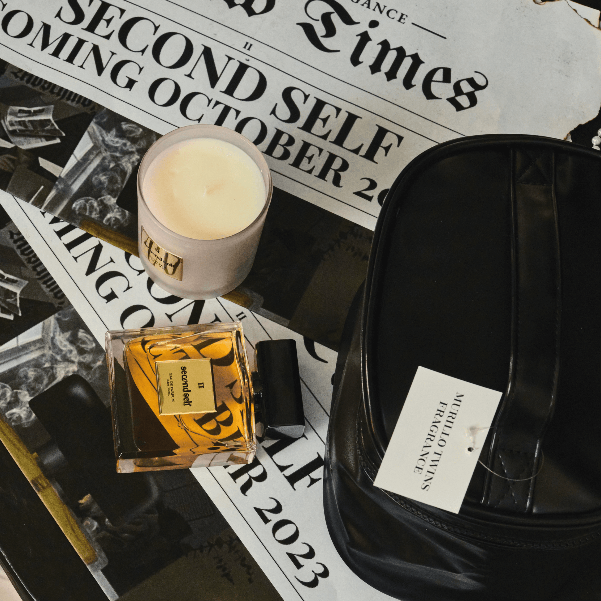 The Second Self Fragrance, Candle, and makeup bag displayed against a backdrop of newspaper clippings.